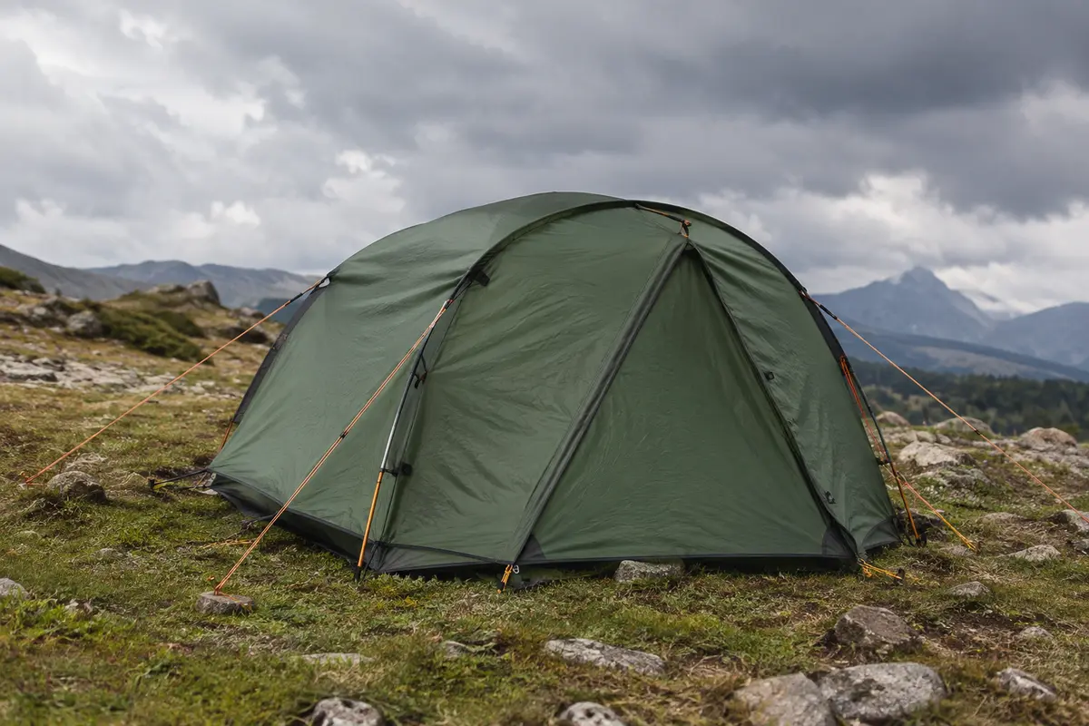 Tente de randonnée montée sur un terrain dégagé, avec arceaux, haubans tendus et toile visibles sous un ciel couvert.
