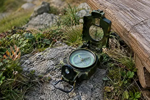 Boussole de randonnée à visée optique et cadran lumineux posée sur un sol minéral en montagne.