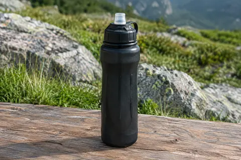 Gourde filtrante noire Bachgold posée sur une table de bivouac en bois, dans un décor de montagne