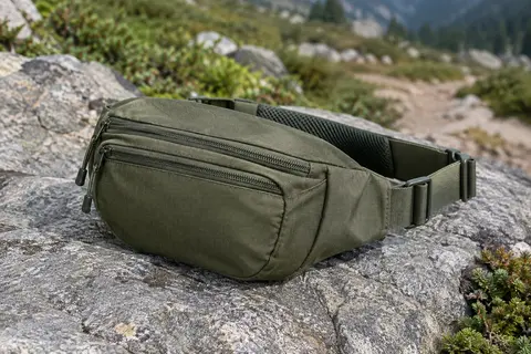 Sac banane Dakine Hip Pack en polyester, avec deux compartiments zippés, posé sur une pierre près d’un sentier.