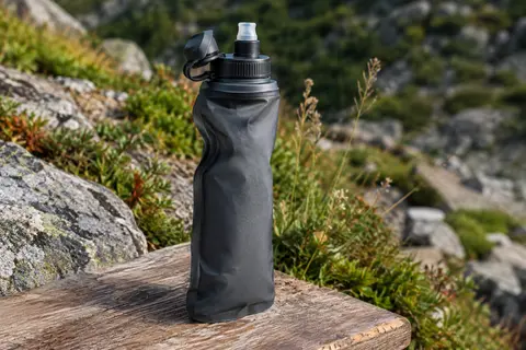 Gourde filtrante compressible gris foncé avec embout, posée sur une table de bivouac en bois brut.