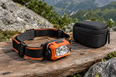 Lampe frontale orange à tête orientable posée sur une table de bivouac en bois brut