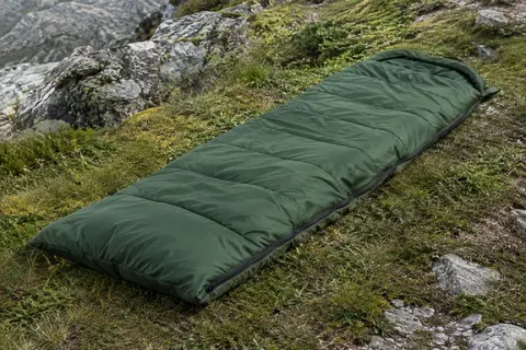 Sac de couchage rectangulaire vert déplié sur l’herbe de montagne, avec sa fermeture éclair visible.