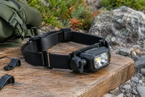 Lampe frontale noire rechargeable posée sur une table de bivouac, avec bandeau élastique et clips de fixation.
