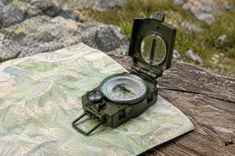 Boussole de randonnée Proster en métal vert armée, ouverte sur une carte posée sur une table en bois