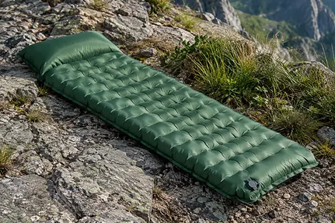 Matelas gonflable vert de randonnée avec oreiller intégré, posé sur un sol minéral en montagne.