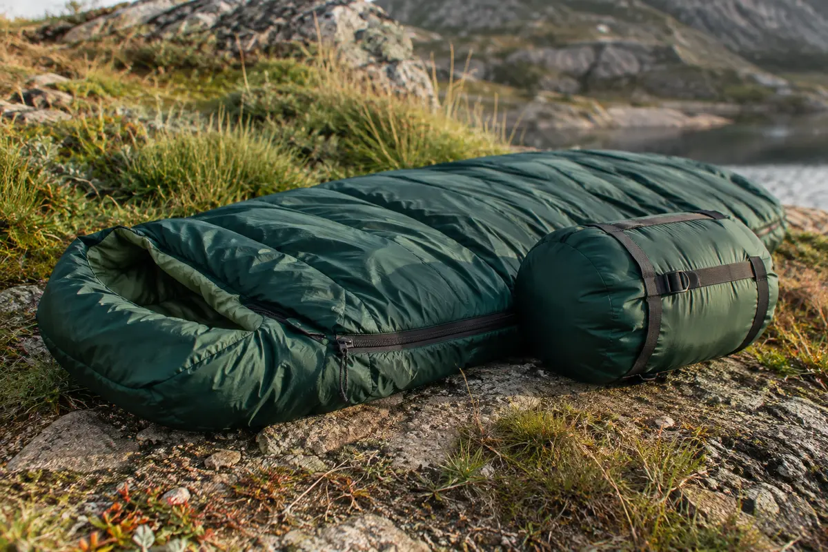 Sac de couchage estival vert posé sur un sol minéral avec son sac de compression