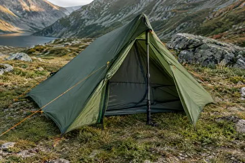 Tente de randonnée verte pour une personne, montée sur un terrain de montagne avec son vestibule ouvert