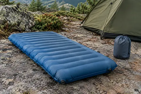 Matelas gonflable bleu Unigear posé sur un sol minéral, avec ses tubes d’air et son sac de transport.