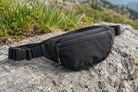 Sacoche banane Waterfly en nylon noir foncé posée sur une pierre grise en extérieur