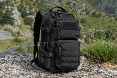 Sac à dos tactique noir de 30 L avec compartiments et poches latérales, posé sur un sol minéral