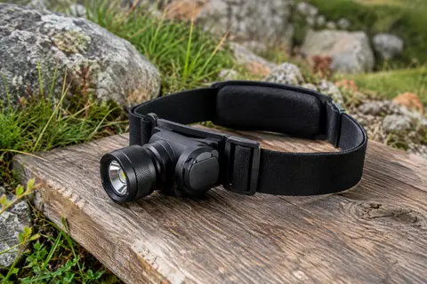 Lampe frontale noire à tête orientable et bandeau réglable posée sur une table de bivouac en bois